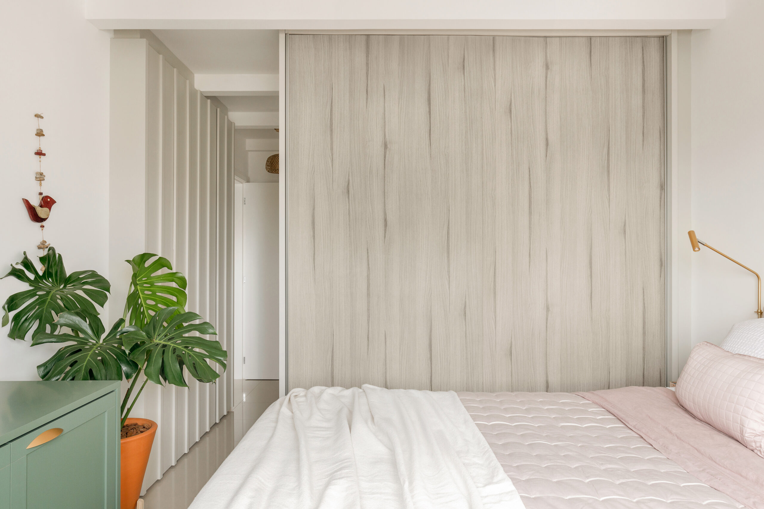 Suíte master com cama casal, guarda-roupa com portas amadeiradas claras e móvel mimetizado estilo ripado no corredor de entrada.