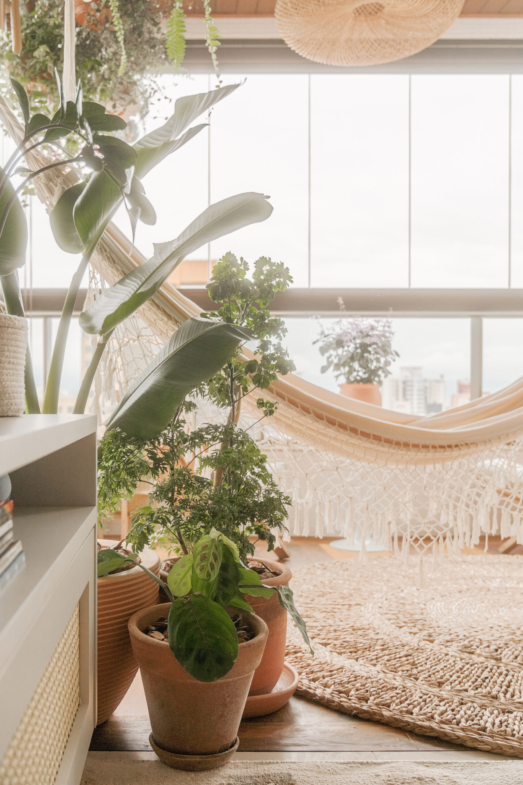 Cantinho acolhedor da sacada integrada no estilo Boho Chic com rede de descanso de macramê, vasos de plantas em terracota e tapete redondo de fibra natural.