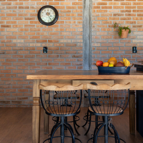 Parede de tijolo maciço aparente na cozinha integrada com mesa de madeira maciça e banquetas de ferro da Casa Lar do Samba