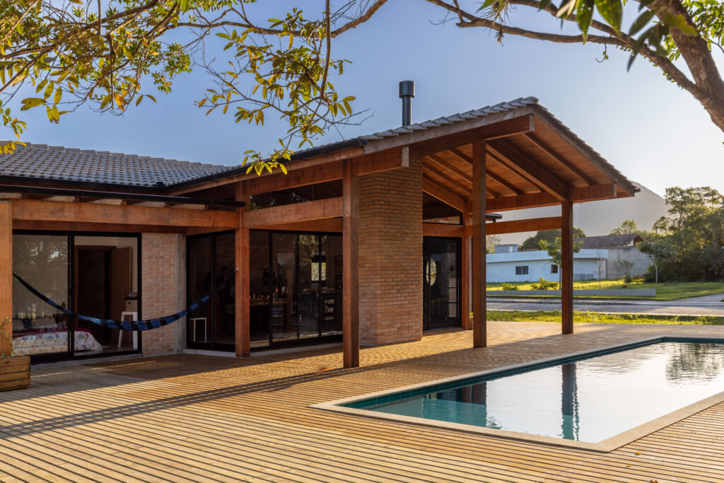 Fachada posterior em ângulo com varanda de madeira aparente, chaminé de tijolo maciço, piscina e deck integrado, Casa Lar do Samba Título: casa-lar-do-samba-fachada-varanda-piscina-angulo